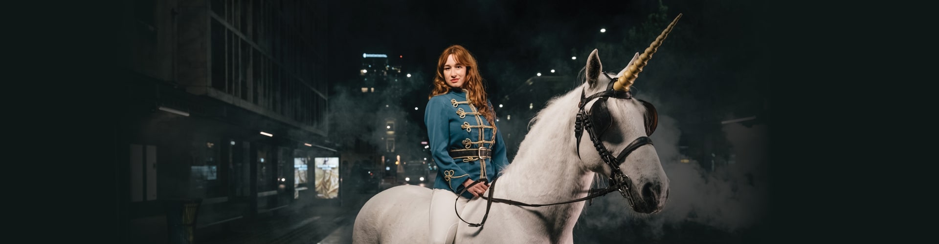 Ženska, ki jezdi belega konja z rogom samoroga v mestu.